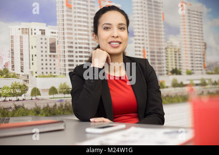 Portrait of cheerful métis woman sitting at desk in office immobilier et looking at camera Banque D'Images