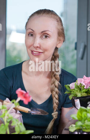 Belle jeune femme avec une tresse pétunia des semis dans des boîtes au printemps. Banque D'Images