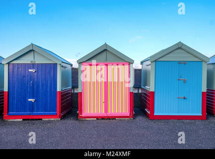 Front de mer de Brighton trois cabines de plage, avec deux portes bleues et celui du milieu a une porte de couleur jaune, rose, rayures noires derrière est b Banque D'Images