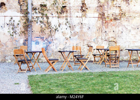 Courtyard Café en plein air avec des tables en bois et une chaise, vert pelouse et ruiné shbby mur sur l'arrière-plan. Ouvrir l'espace aérien. Fusion de st Banque D'Images