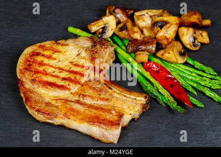 Steaks de porc aux herbes, asperges, champignons sur fond ardoise close up. Sex plats de viande. Vue d'en haut Banque D'Images