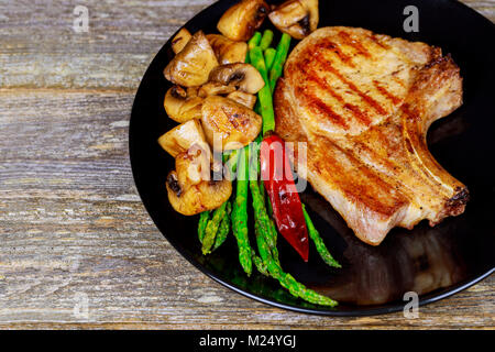 Steaks de porc aux herbes, asperges, l'ail, les champignons fond noir sur fond de bois de près. Banque D'Images