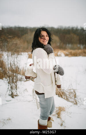 Femme souriante avec une paire de patins à glace sur une épaule et les cheveux balayés par Banque D'Images