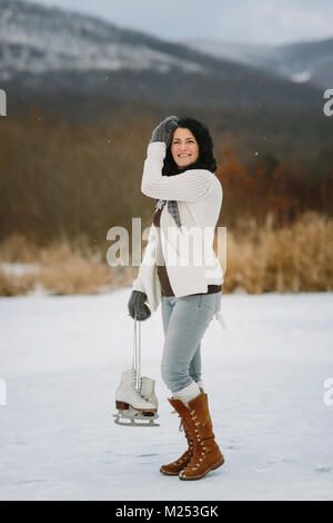 Femme souriante avec une paire de patins à glace et les cheveux balayés par Banque D'Images