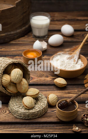 En forme de noix délicieux biscuits shortbread rempli de lait condensé sucré et les pistaches hachées sur argile brun plat. sur l'ancien fond de bois, vue de dessus, close-up Banque D'Images