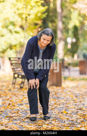 Senior woman walking in autumn park et d'avoir une douleur au genou. Concept de douleur d'arthrite. Banque D'Images