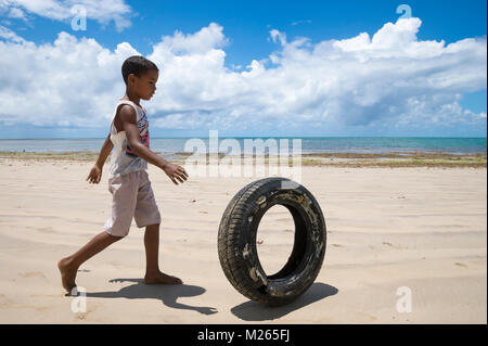 Fernando Machado, BRÉSIL - 15 février 2017 - Un garçon Brésilien un pneu roule comme un jeu le long d'une plage éloignée à Bahia. Banque D'Images