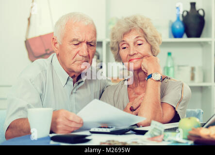 Couple frustrés face à des ennuis financiers table avec titres, espèces et calculatrice Banque D'Images