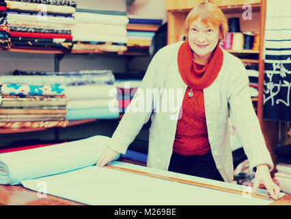 Vendeuse mature mesure le tissu dans un magasin de tissu Banque D'Images