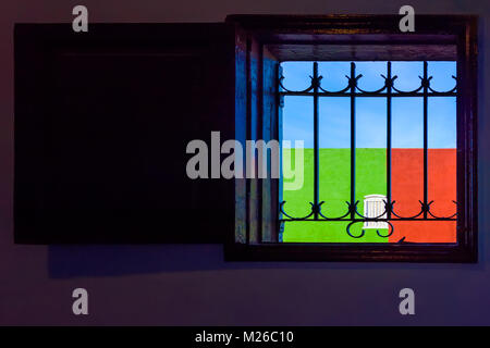 Un Cubain typique fenêtre avec un treillis et une vue sur le mur rouge-vert avec une fenêtre blanche et un ciel bleu Banque D'Images