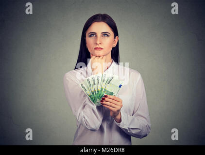 Jeune brunette holding pile d'argent et à l'écart, songeur. Banque D'Images