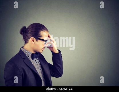 Man in suit concentré tout en frottant le front pensif et à la recherche d'idées†loin sur fond gris. Banque D'Images