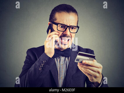 Jeune homme parlant au téléphone tout en maintenant les cartes de crédit et les disputes expressive. Banque D'Images