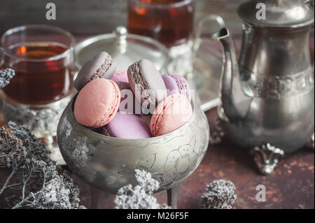 Des petits macarons sur plaque de métal avec de petites fleurs blanches et de thé composition appareils sur fond de bois. Focus sélectif. Banque D'Images