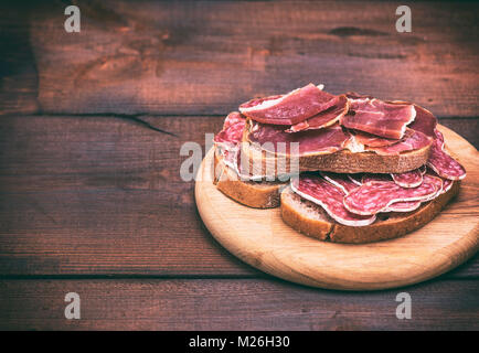 Avec des sandwichs saucisse fumée de salami et de pièces d'hamon sur une table ronde en bois, espace vide sur la gauche Banque D'Images