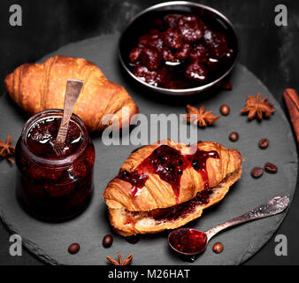 La confiture de fraise dans un bocal en verre et croissant frais sur un fond noir, vue du dessus Banque D'Images