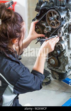 Une jeune femme portant des gants blancs utilise une clé, le remplacement de la courroie de distribution sur un moteur de voiture. Banque D'Images