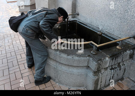 L'homme de boire l'eau minérale en continu à partir d'un appuyez sur Jour et nuit devant les bains minéraux bâtiment dans la ville de Sofia, capitale de Bulgarie. fontaine d'eau potable Banque D'Images