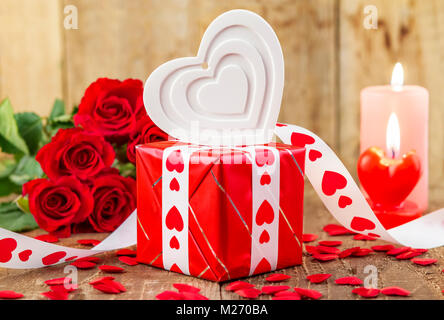 Forme de coeur blanc plus de boîte-cadeau en face de bouquet de roses rouges et des bougies sur fond de bois. Valentines Day concept. Mère jour concept. Banque D'Images