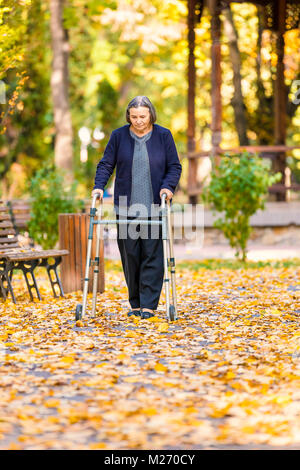 Senior woman with walker walking outdoors in autumn park. Banque D'Images