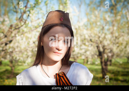 Jeune fille en uniforme de la Grande guerre patriotique. Guerrier assis sur l'herbe entre les fleurs. Girl wearing costume vert de la Seconde Guerre mondiale Banque D'Images