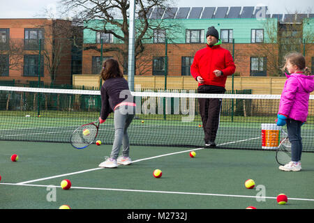 Session d'entraînement de tennis pour enfants / leçon ayant lieu sur un court de tennis avec les enfants / kids et entraîneur de tennis professionnel, en hiver. UK Banque D'Images