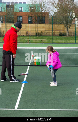 Session d'entraînement de tennis pour enfants / leçon ayant lieu sur un court de tennis avec les enfants / kids et entraîneur de tennis professionnel, en hiver. UK Banque D'Images