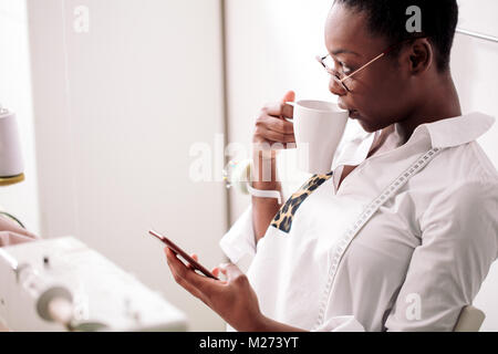 Cheerful woman couturière tablier en parlant au téléphone et de boire du café Banque D'Images