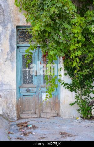 Oublié abandonnés à une porte d'entrée en Grèce accueil peints en bleu avec de la peinture et du feuillage grandit la porte et mur Banque D'Images