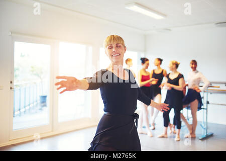 Smiling senior woman doing danse classique dans un studio de danse avec un groupe d'amis dans l'arrière-plan Banque D'Images