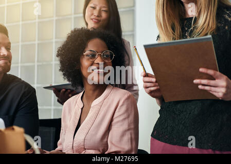 Groupe diversifié de smiling collègues parler tout en travaillant ensemble autour d'une table dans un bureau moderne Banque D'Images