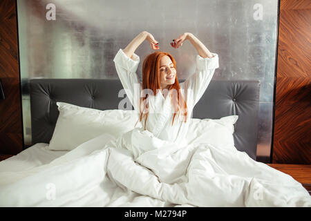Redhead Woman stretching au lit après le réveil Banque D'Images