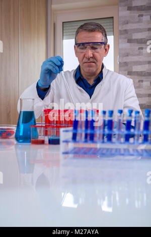 L'ajout de solution scientifique les tubes à essai en laboratoire. Les produits chimiques de laboratoire tubes à essai en verre avec un liquide rouge et bleu.homme porte des lunettes et Banque D'Images