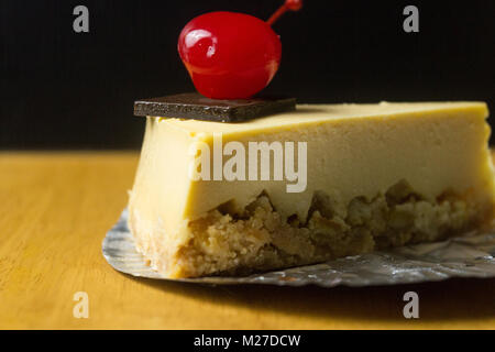 Morceau de gâteau au fromage avec cerise sur fond sombre et de tables en bois Banque D'Images