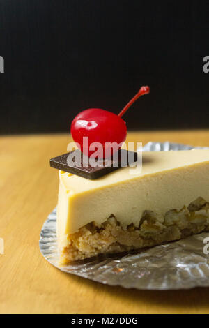 Morceau de gâteau au fromage avec cerise sur fond sombre et de tables en bois Banque D'Images