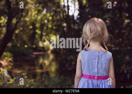 Petite fille, je suis debout dans la contemplation et à la recherche vers une rivière calme, Woodland Banque D'Images