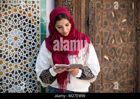 Femme arabe en costume traditionnel avec hijab rouge sur sa tête la lecture d'un livre Banque D'Images