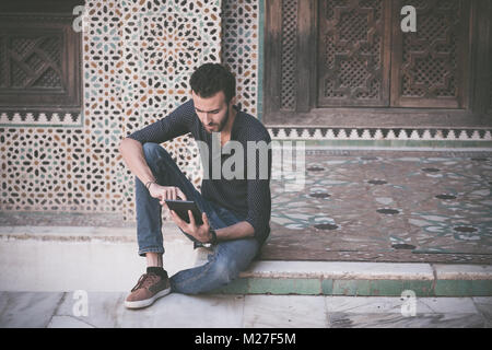 Jeune musulman dans l'habillement occasionnel travaillant sur le comprimé dans l'arabe traditionnelle Banque D'Images