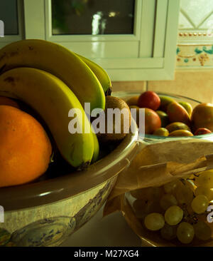Beau millésime coupe de fruits et sac de papier avec de nombreux fruits : bananes, kiwis, oranges, raisins et les tomates. Scène d'intérieur d'une maison rurale. Banque D'Images