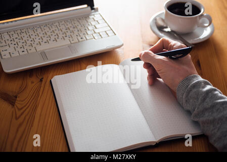 La main de l'homme écrit dans Planner. Le café, ordinateur portable en arrière-plan Banque D'Images