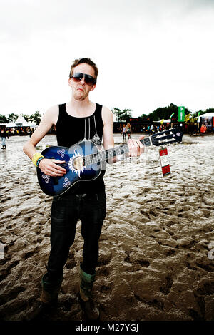 Un festival à Roskilde Festival joue sa guitare au milieu d'une zone du festival boueux. Banque D'Images