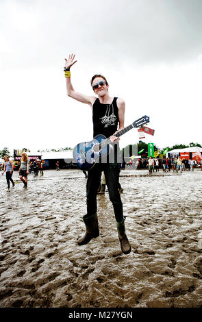 Un festival à Roskilde Festival joue sa guitare au milieu d'une zone du festival boueux. Banque D'Images