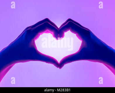 Les mains dans la forme de coeur fond rouge. le symbole de coeur avec la main. valentines day card. Woman's hands silhouette en forme de cœur. Banque D'Images