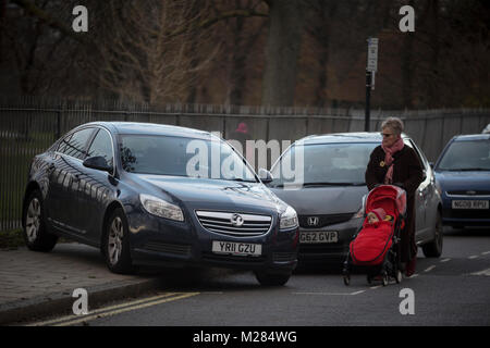 Une vieille dame avec un buggy enfant marche dans la route, après un repos voiture Vauxhall abandonné mystérieusement à 45 degrés, de la route mais le blocage d'une chaussée de Ruskin Park, le 2 février 2018, à Southwark, Londres, Angleterre. Parce que la voiture n'est pas de bloquer l'autoroute, ce n'est pas une affaire de police - mais causant un obstacle sur la chaussée en fait un problème du conseil. Banque D'Images