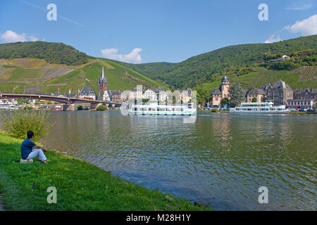 Femme assise à la Riverside et regarder les bateaux d'excursion sur la Moselle, Bernkastel-Kues, Moselle, Rhénanie-Palatinat, Allemagne, Europe Banque D'Images