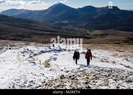 Randonnée Les randonneurs jusqu'à la colline sur chemin Rhyd Ddu sur les bas des pentes du Mont Snowdon avec de la neige en hiver dans le parc national de Snowdonia. Gwynedd, au nord du Pays de Galles, Royaume-Uni Banque D'Images