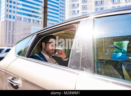 Young businessman sitting dans la banquette arrière d'une voiture l'utilisation d'un cellulaire tout en roulant à travers la ville Banque D'Images