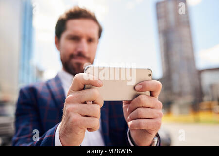 Libre d'un jeune homme vêtu d'un blazer tout seul dans une rue de la ville à l'aide d'un smartphone Banque D'Images