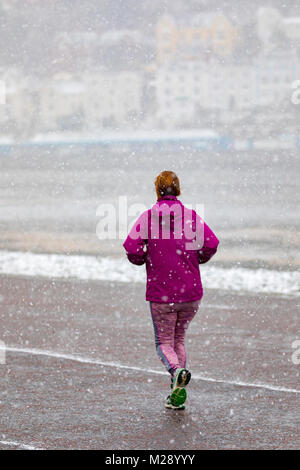 Llandudno, au Pays de Galles, le 6 février 2018. Météo britannique. Comme prévu un avertissement jaune pour la neige pour le Nord du Pays de Galles aujourd'hui avec certaines parties recevant jusqu'à 8 cm sur un terrain plus élevé. La neige très inhabituelle pour la station balnéaire de Llandudno dans le Nord du Pays de Galles comme cette personne a découvert le jogging le long de la mer © DGDImages/Alamy Live News Banque D'Images