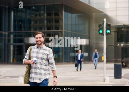 Certain jeune homme souriant et de boire une tasse de café tout en profitant d'une marche seul à travers la ville Banque D'Images